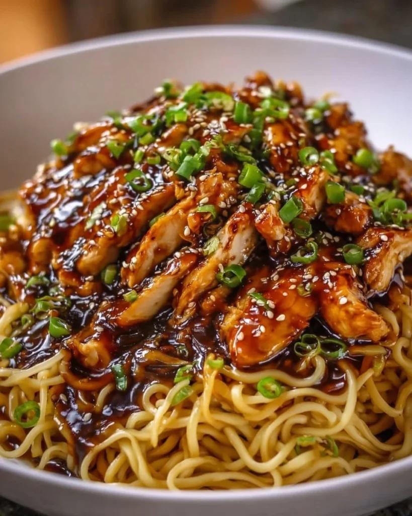 Plate of sticky garlic chicken noodles topped with fresh herbs